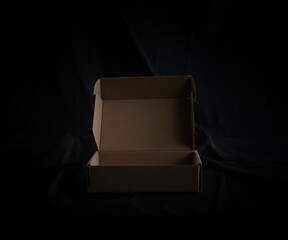 Open empty cardboard box and black luxury fabric table top background and texture
