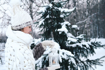 A happy woman stands with a lantern in her hands, a winter park with snow-covered trees