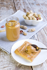 Peanut butter in a glass jar with a napkin on a wooden background. Delicious and healthy breakfast.