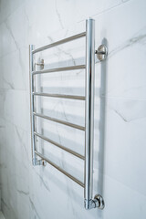 Wall-mounted towel dryer in the shower room. Marble white walls in the bathroom. Metal heated towel...