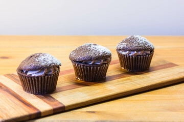Three Chocolate Victoria Sponge Mini Cup Cakes Filled with Cocoa Cream and Dusted with Sugar on Cherry Wooden Board