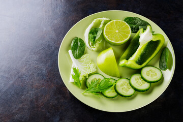 Organic green vegetables and fruits on a dark background. Green diet food on a plate. Healthy food. Top view. Copy space