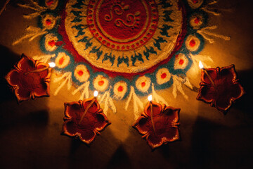 Diwali Celebrations- Clay Diya lamps lit around rangoli during Diwali, Hindu festival of lights celebration. Colorful traditional oil lamp diya on rangoli background.