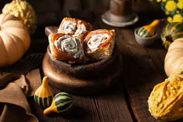 Homemade cinnabons with pumpkin cream and vanila cream on wooden background with raw pumpkins,yellow flowers and ceramic dishes.