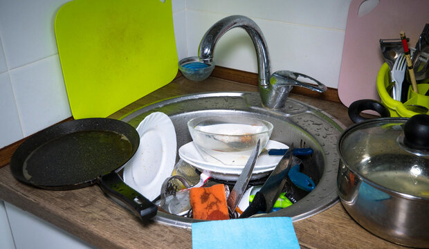 A lot of dirty dishes in the kitchen sink, huge heap of dirty dishes waiting for the flatmate