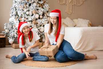 Sisters celebrate winter holidays. Girls exchange Christmas gifts near Christmas tree. Happy among New Year's decor. 