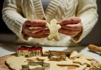 Close up of chef's hands holding a man shaped cut out gingerbread dough while making Christmas cookies in the kitchen