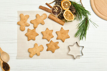 Gingerbread cookies as stars shape for Christmas, on a parchment paper with pine cones and branches, dried slices of orange and cinnamon sticks