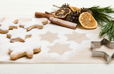 Baked star-shaped gingerbread cookies powdered with sugar for Christmas on baking parchment paper near pine cones and twigs, dried orange slices and cinnamon sticks - Powered by Adobe