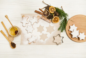 Baked star-shaped gingerbread cookies powdered with sugar for Christmas on baking parchment paper near pine cones and twigs, dried orange slices and cinnamon sticks. Flat lay