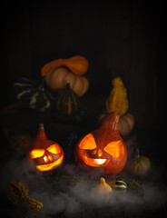 Naklejka premium Halloween scene with burning pumpkins,smoke and raw vegetables on dark wooden background.