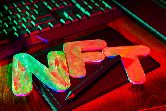 NFT Non-Fungible Token text of letters illuminated with neon light. Workplace of a graphic designer creating NFT digital art. Concept of cryptoart and blockchain technology