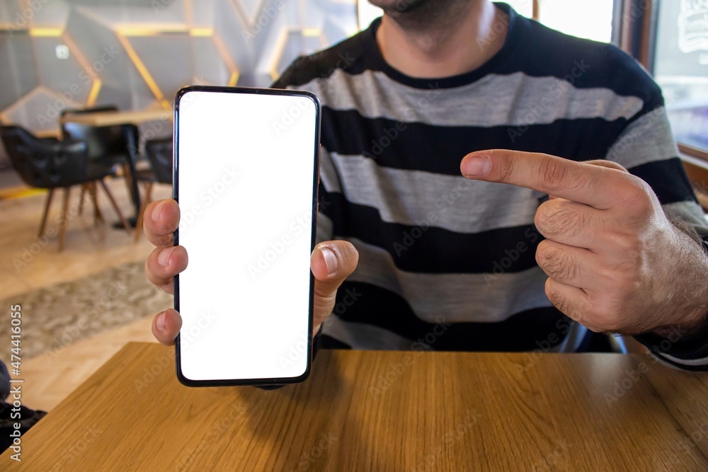 Poster man showing mobile phone with blank white screen while sitting in a cafe.