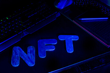 NFT Non-Fungible Token text of letters illuminated with blue neon light. Workplace of a graphic designer creating NFT digital art. Concept of cryptoart