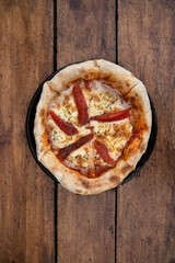 Top view of a pizza with mozzarella cheese and roasted bell pepper slices, on the wooden table.