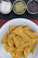 Mexican food. Top view of nachos in a white bowl and three dipping sauces of cheddar cheese, sweet chili and guacamole. 