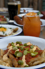 Ready to eat. View of french fries with broad beans and spicy sauces at the restaurant table. Other dishes, beer and tropical cocktails in the background.