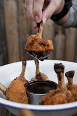 Eating. Closeup view of a hand holding a fried chicken wing dipped in bittersweet sauce. 