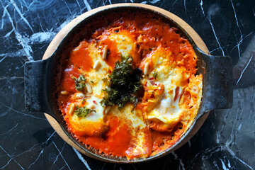 eggs shakshuka in a frying pan on a table, top view - obrazy, fototapety, plakaty