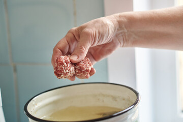 A woman's hand tosses a couple of meatballs into a pot of boiling soup. Healthy home cooking.