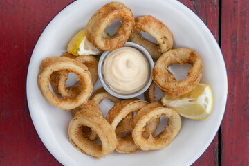 Deep fried seafood. Top view of delicious fried squid rings with lemon and a dipping sauce in a white bowl.