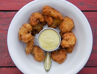 Seafood. Overhead view of fried breaded shrimps with avocado mayonnaise and lemon in a white bowl on the red wooden table.