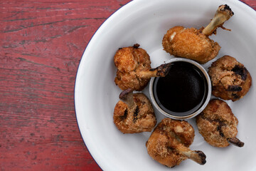 Top view of deep fried breaded chicken wings with a bittersweet dipping sauce, in a white bowl on the red wooden table. 