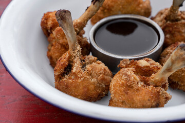 Fast food. Closeup view of deep fried breaded chicken wings with a bittersweet dipping sauce, in a white bowl on the red wooden table.