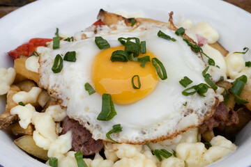 Closeup view of fried potatoes with melted cheese, chorizo, bell pepper, onion and a grilled egg in a white dish.  