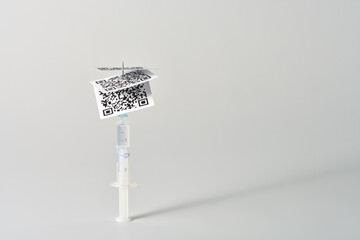  A syringe with QR codes impaled on a needle on a white background. Copy space.