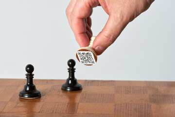 A man's hand rearranges a chess piece with a QR code on the chessboard. Copy space.