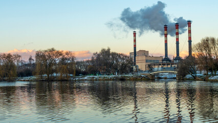 Obraz premium Smoking chimneys of thermal power plants near the waterfront in city. Winter. Industrial and nature background.