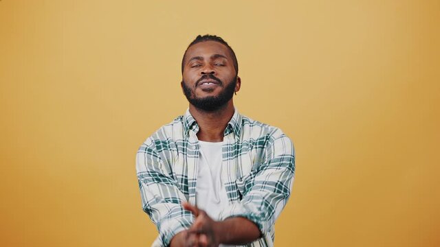 Young African American man is crossing fingers acting like praying for luck. Shaking clenched fists, looking unhappy. Posing on beige background