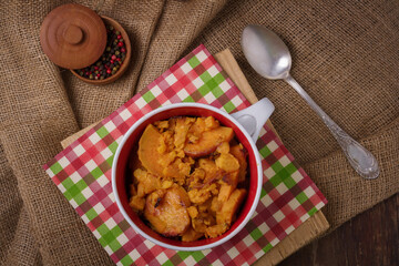 Bowl on burlap with stewed sweet potatoes or yam. Tasty nutricious dish, healthy country food. Pepper peas spice pot, spoon.