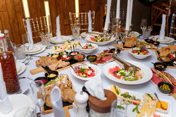 Festive table setting with vegetable salads, meat, cheese, bread and drinks. Family event celebration, anniversary, wedding or birthday.
