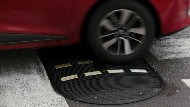Cars on a speed bump before crosswalk. Wheels of the vehicles going over road hump on the street, used to slow down the traffic for pedestrians' safety. Stop line and zebra crossing marked on asphalt.