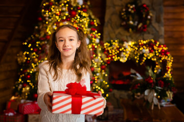Merry Christmas. A young girl holds a gift against the background of a Christmas tree. The girl laughs and enjoys the gift.