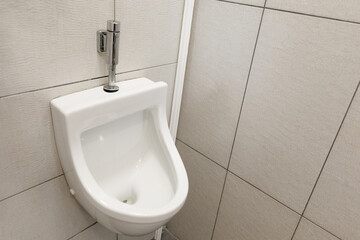 Men's room in the toilet, white tiled urinal on the wall.