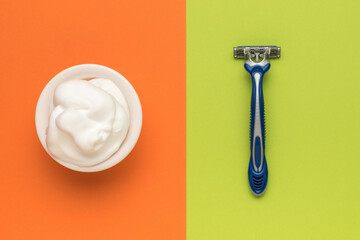 A bowl filled with shaving foam and a disposable razor on a green-orange background. Flat lay.