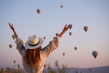 Tourist girl standing and looking to hot air balloons in Cappadocia, Turkey.Happy Travel in Turkey concept.Woman on a mountain top enjoying wonderful view of sunrise and balloons.    