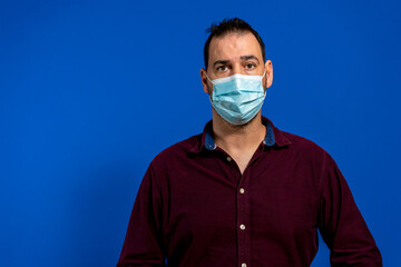 Portrait of handsome young businessman with surgical medical mask looking at camera. Business people medicine and health care concept. Indoor, studio shot on blue background.