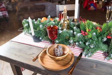 Elegant Christmas dinner table setting. Decoration of Christmas table: candles, juniper branches and napkins, wooden plates. New Year decorations in living room.country style.