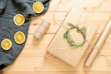 Fototapeta na wymiar Concept of idea, eco friendly materials for wrapping Christmas gifts. Craft box, whip, green twigs, wrapping paper, dried orange, muslin cloth on wooden table. DIY. Step-by-step instruction. Step 6