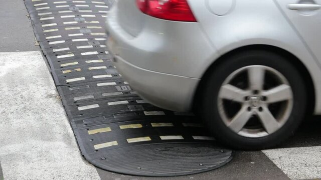 Cars on a speed bump before crosswalk. Wheels of the vehicles going over road hump on the street, used to slow down the traffic for pedestrians' safety. Stop line and zebra crossing marked on asphalt.