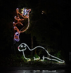 Colored Christmas lights and  holiday lights, depicting a seal chasing a racoon up a tree at a zoo...