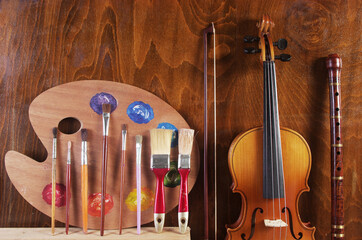 Attributes of the arts. Art palette, brushes, violin, bow, pipe on a wooden textured background.