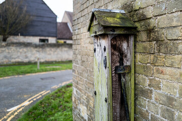 Very old and decayed village water pump and faucet seen on the side on a building at the junction of an English village. Showing part of the old wooden housing of the pump.