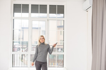 Happy Woman Holding Remote Control In Front Of Air Conditioner At Home