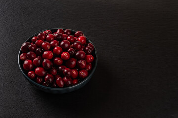 Fresh red cranberries in a bowl over black background with space for text. Ingredient for cooking Thanksgiving and Christmas dishes and desserts. Organic wild berries for vitamin healthy eating.