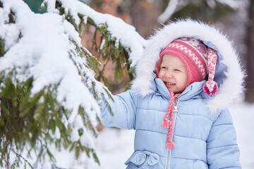cute smiling girl is standing under a snow tree. He pulls a snowy branch and has fun.